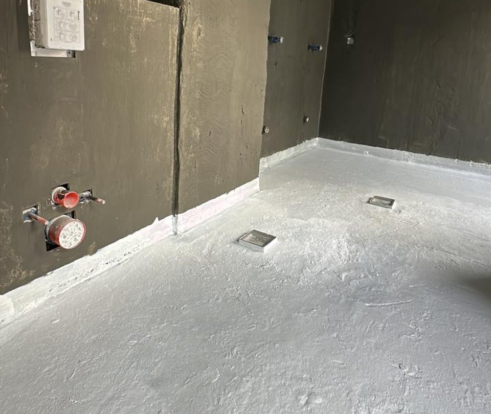 Bathroom before: bare walls, exposed plumbing points and white waterproofing membrane on the floor
